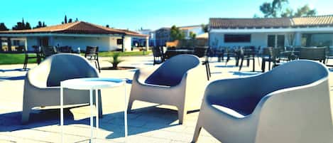 A patio area with modern chairs and tables, a small round table, and a building with a tiled roof in the background.