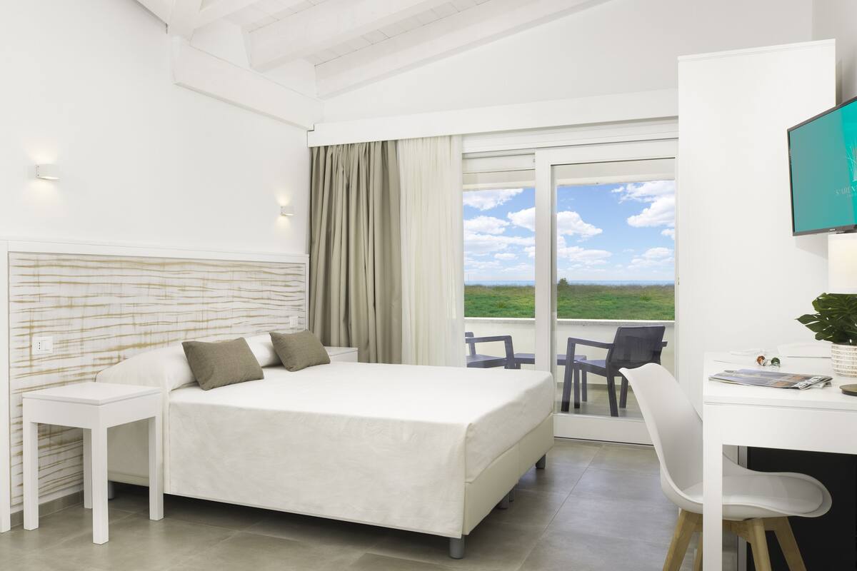 A modern hotel room with a bed, a desk, and a view of the outdoors.