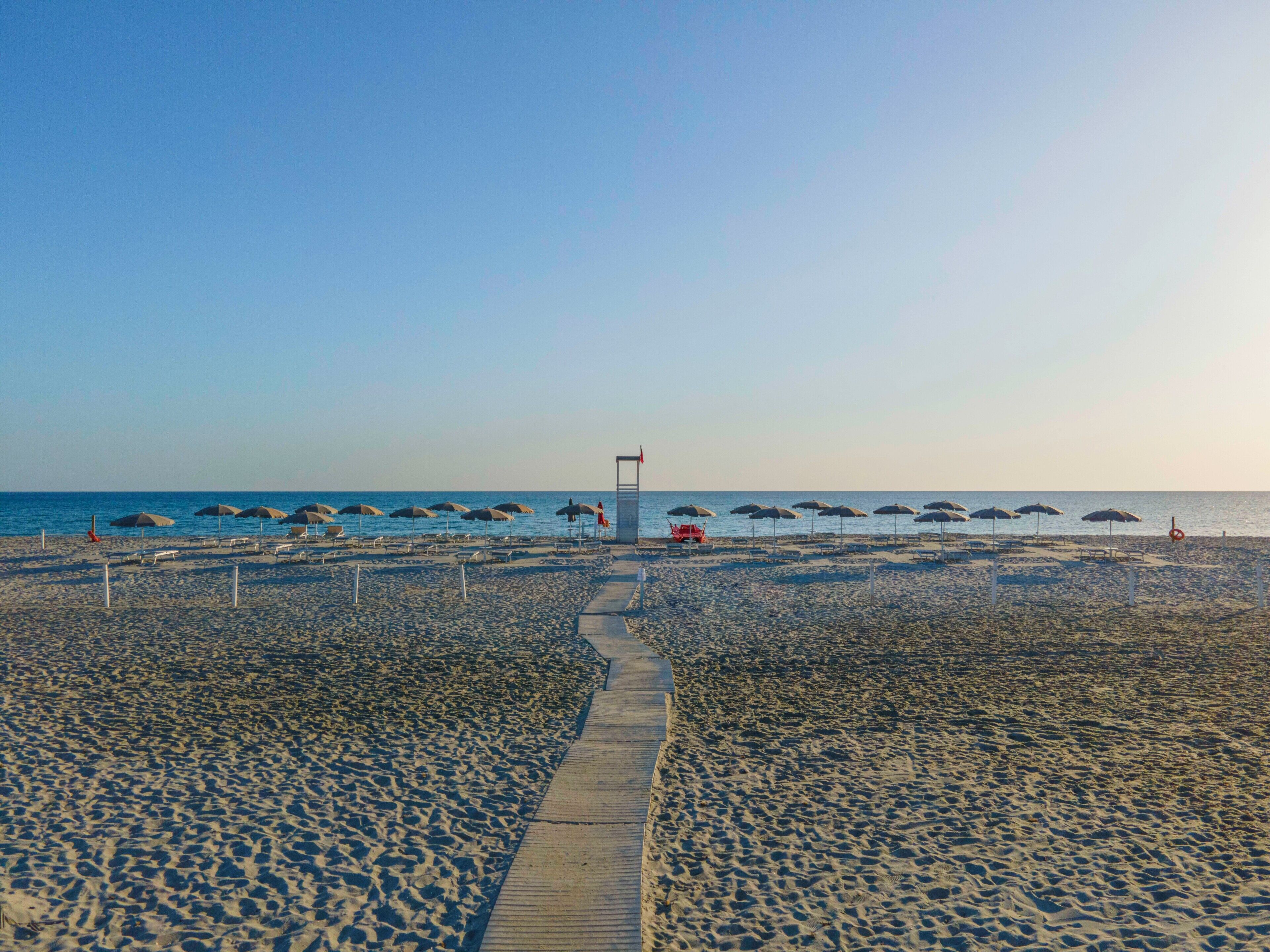 Een strand met een pad naar de zee, parasols en strandstoelen.