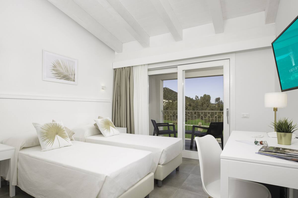 A hotel room with two beds, a desk, a chair, a TV, and a balcony with a view of the outdoors.