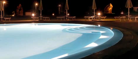A swimming pool with a lighted edge, lounge chairs, and umbrellas.