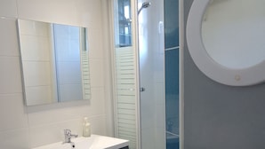 Une salle de bain moderne avec un lavabo blanc, un meuble-lavabo foncé, un miroir, une douche et un lave-linge.