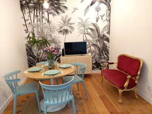 Un coin repas avec une table ronde, des chaises bleues, une chaise rouge et un téléviseur posé sur un meuble.