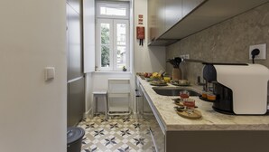 Una cocina con un refrigerador de acero inoxidable, una cafetera y una ventana que ofrece vistas a edificios.