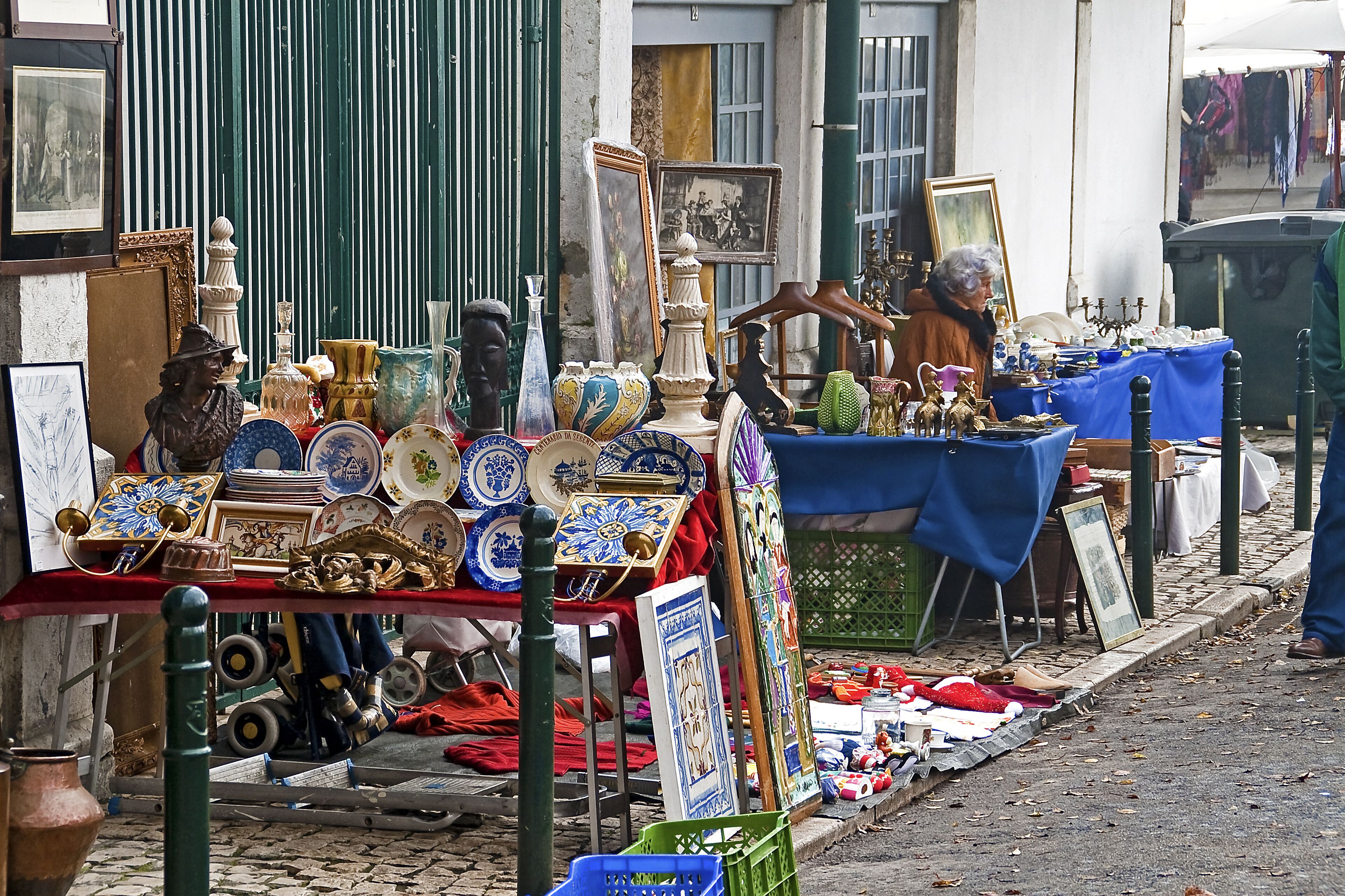 A street market with various items for sale, including pottery, framed pictures, and decorative objects.