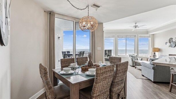 Un coin repas avec vue sur l’océan, des chaises en osier, une table en bois et un luminaire suspendu.
