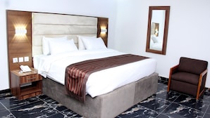 A hotel room with a large bed, a nightstand with a phone, a chair, and a mirror on the wall. - K-class Hotel (Abuja)