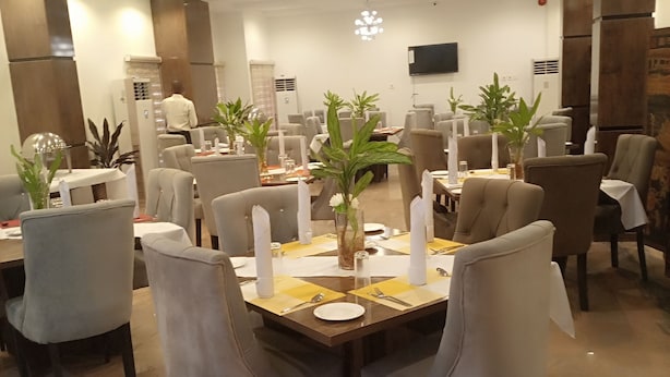 A dining area with multiple tables, chairs, and potted plants. - K-class Hotel (Abuja)