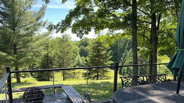 Una terraza de madera con una mesa redonda y sillas, con vistas a un área verde con árboles.