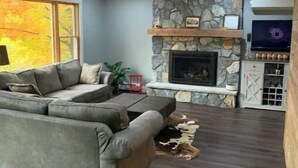 Una sala de estar moderna con chimenea de piedra, un amplio sofá seccional gris y un televisor de pantalla plana montado sobre la chimenea.