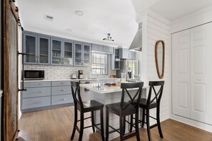Una cocina moderna con armarios grises, una isla blanca y taburetes negros.