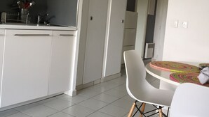 Moderni keittiö, jossa on valkoiset kaapit, ruokailutila pyöreän pöydän ja kahden tuolin kera sekä käytävä, joka johtaa toiseen huoneeseen.