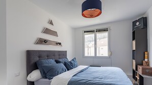 Un dormitorio moderno con una cama grande, un cabecero gris y una ventana con vistas a casas.