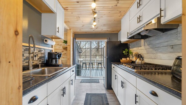 A modern kitchen with white cabinets, a black countertop, and a wooden ceiling. - 🔥hot tub, view, 🐕 friendly modern cabin (New Market)