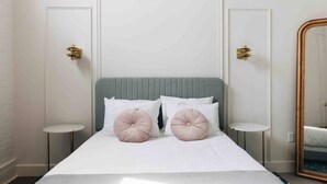 A neatly made bed with a grey headboard, two bedside tables with gold accents, and a large mirror with a gold frame.