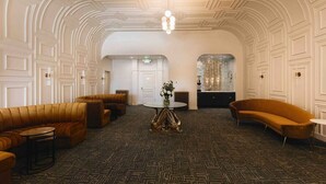 A spacious lobby with a patterned carpet, a central round table with a vase of flowers, and a modern chandelier.