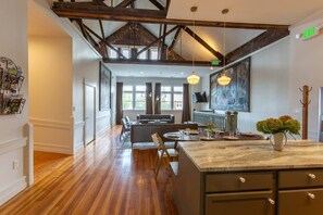 A spacious kitchen with a marble countertop, wooden flooring, and a high ceiling with exposed beams.