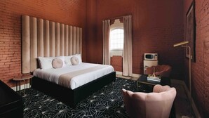 A modern bedroom with a brick wall, a large bed with a headboard, a small table, and a chair.