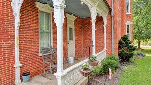 A red brick building with a white porch, a door, and a window. There is a chair, a bucket, and a potted plant on the porch. - The Ole Farmhouse at Warm Springs  - Country Living For the Whole Family (Landisburg)