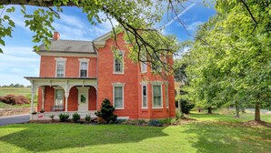 A large, two-story brick house with a front porch, surrounded by well-maintained lawns and trees. - The Ole Farmhouse at Warm Springs  - Country Living For the Whole Family (Landisburg)