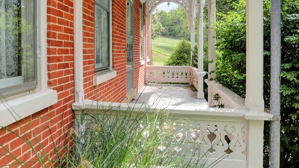 A brick building with a porch featuring a white railing and a blue awning. - The Ole Farmhouse at Warm Springs  - Country Living For the Whole Family (Landisburg)