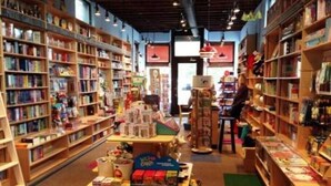 A bookstore with bookshelves on both sides, a central display table with various items, and a person browsing. - Glenmary Suite 204 at The Bellwether Hotel (Louisville)