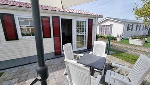 Eine Terrasse mit Tisch und Stühlen, eine Glastür zum Verschieben und ein kleiner Garten mit Blumentöpfen.
