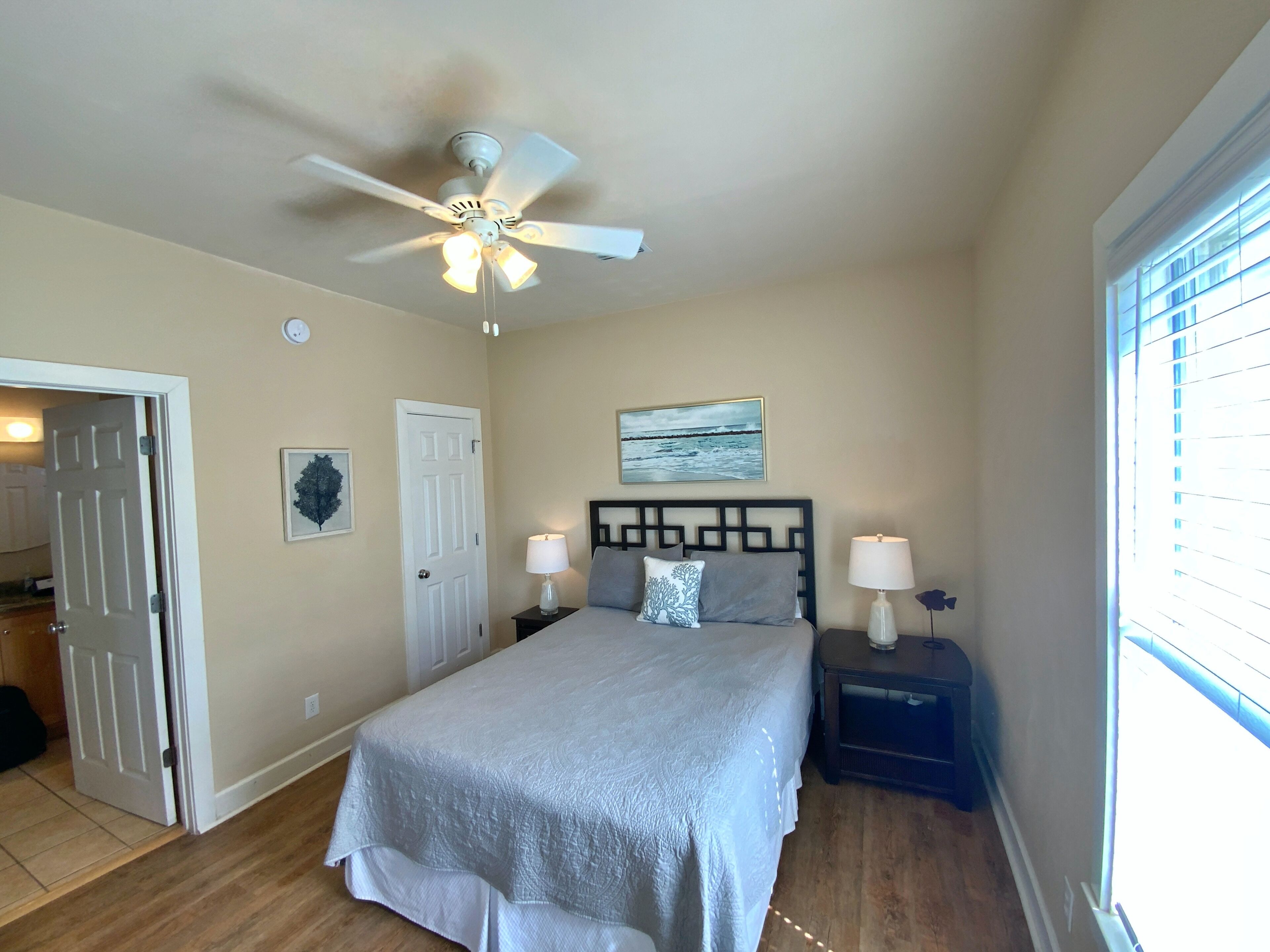 A bedroom with a bed, two bedside tables with lamps, a ceiling fan, a door, and a window.