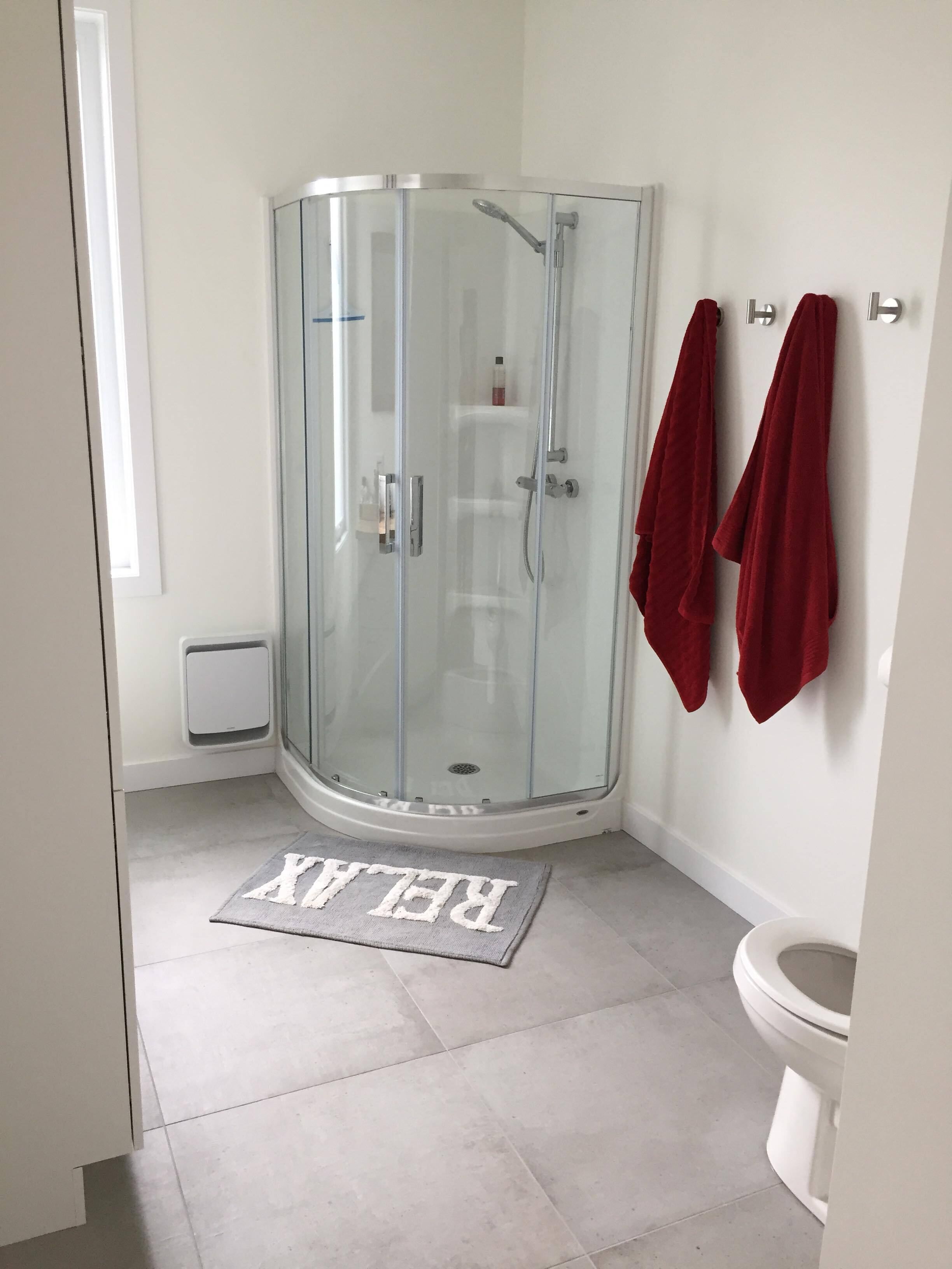 A modern bathroom with a glass shower enclosure, a toilet, and a red towel rack.