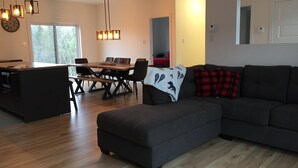 A modern living room with a dark grey sofa, a wooden dining table with chairs, and pendant lights.