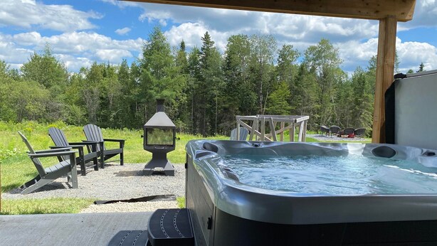 An outdoor hot tub area with a wooden deck, two Adirondack chairs, and a wooden pergola.
