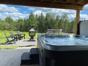 Ein Außenbereich mit Whirlpool, einer Holzterrasse, zwei Adirondack-Stühlen und einer Holzpergola.