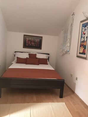 A bedroom with a bed, a painting, and a window with a curtain.