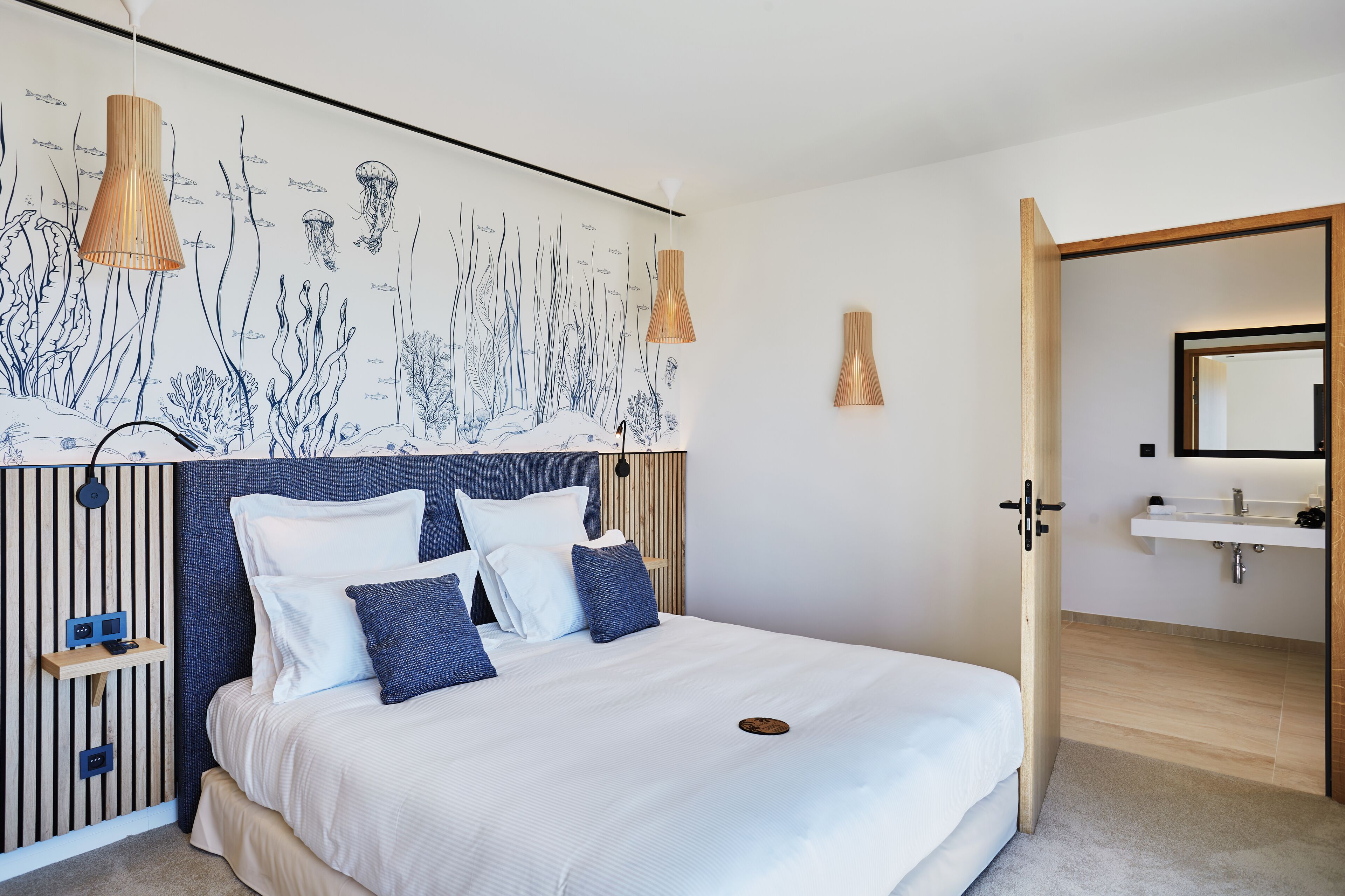 Un dormitorio con una cama grande, un mural en la pared, una mesita de noche y un baño visible a través de una puerta abierta.