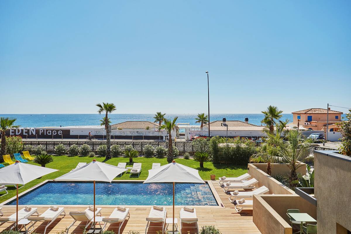A pool area with lounge chairs and umbrellas, a clear view of the sea, and a sign reading "EDEN PLACE".