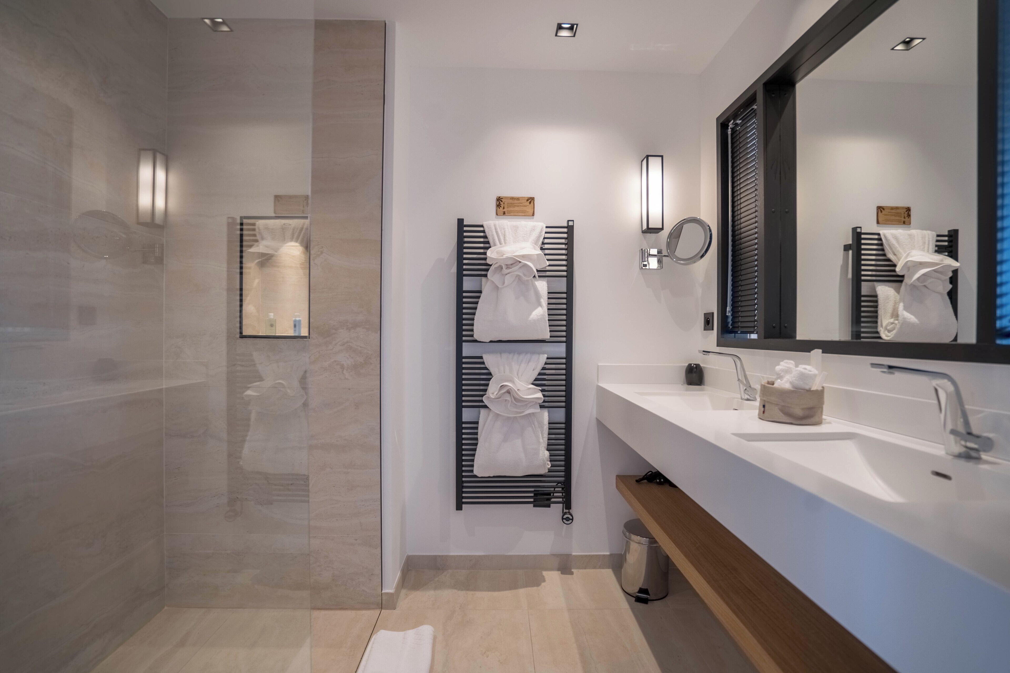 A modern bathroom with a glass shower enclosure, a large mirror, and a wooden vanity with a sink.