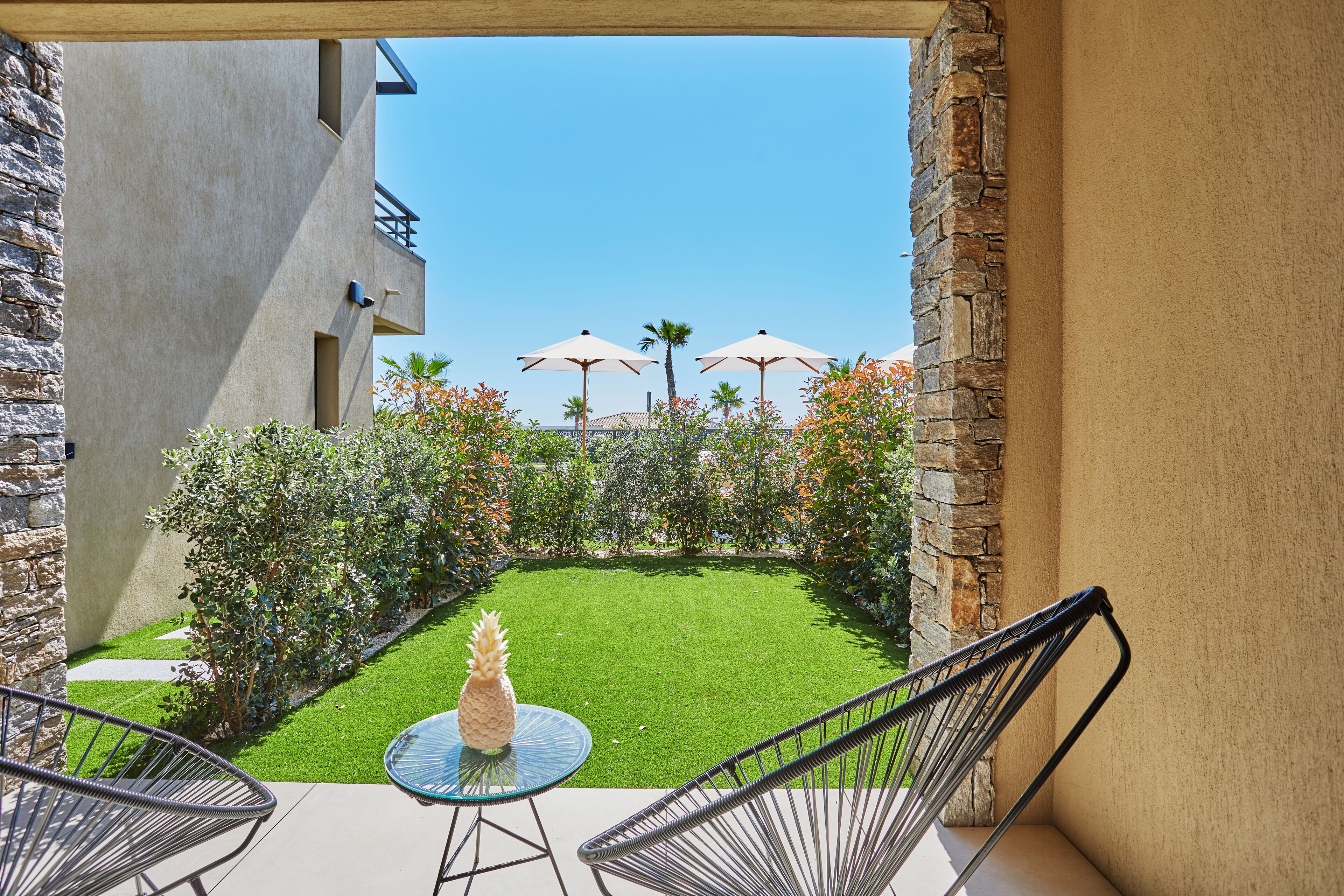 A patio with a glass table and metal chairs, overlooking a well-maintained lawn and stone walls.