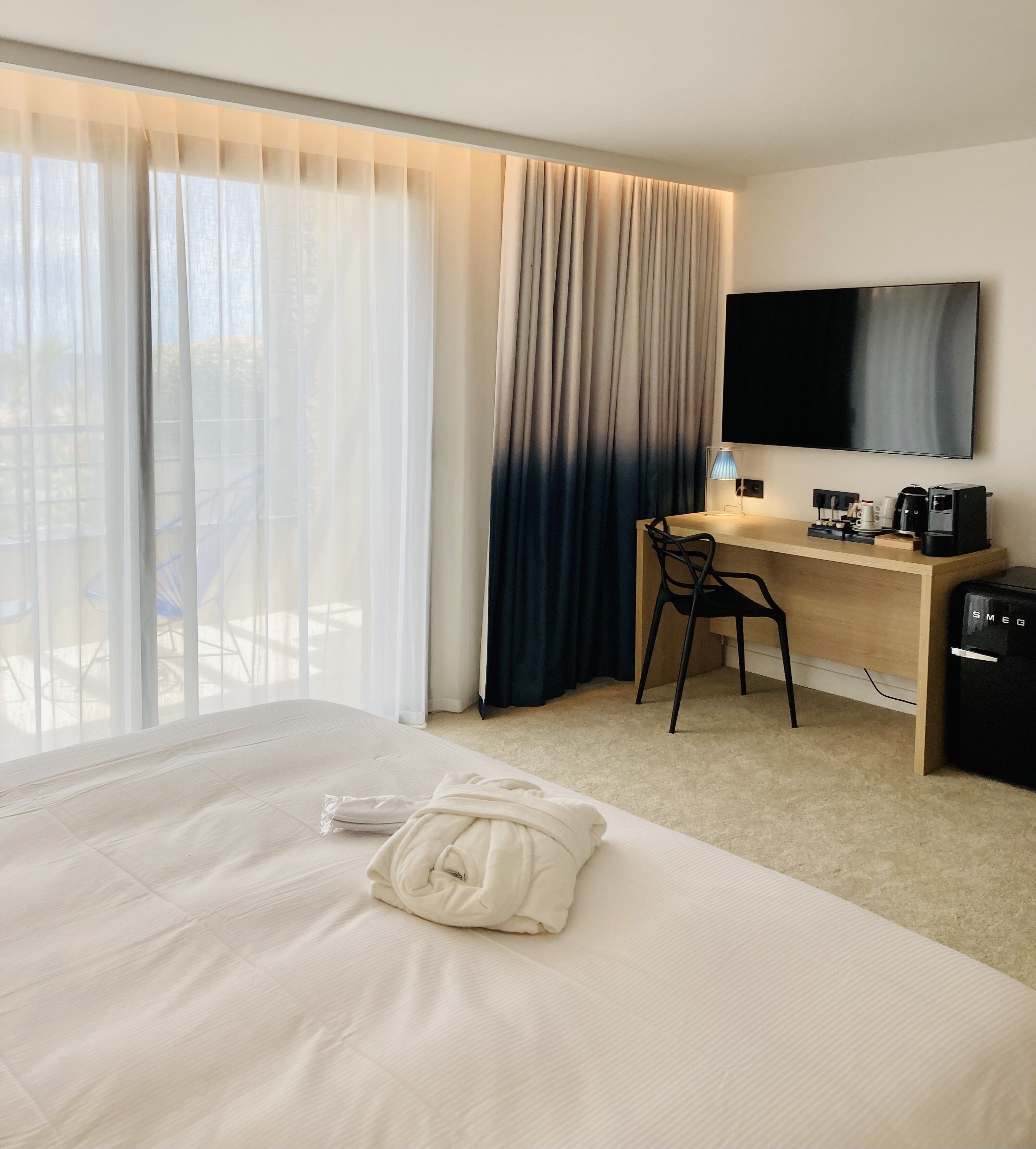 A hotel room with a large bed, a desk with a chair, a television, and a coffee machine.