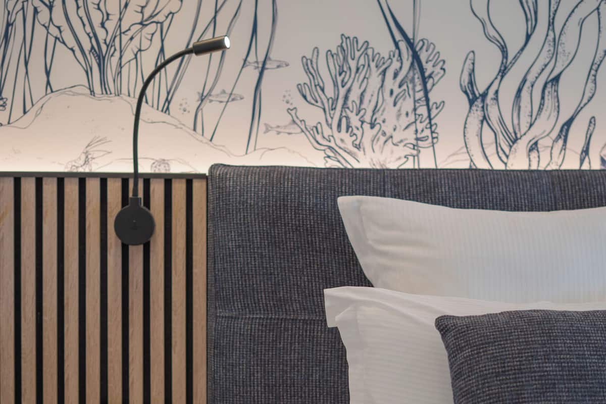 A bedroom with a bed, a wall-mounted lamp, and a wooden panel with a switch.