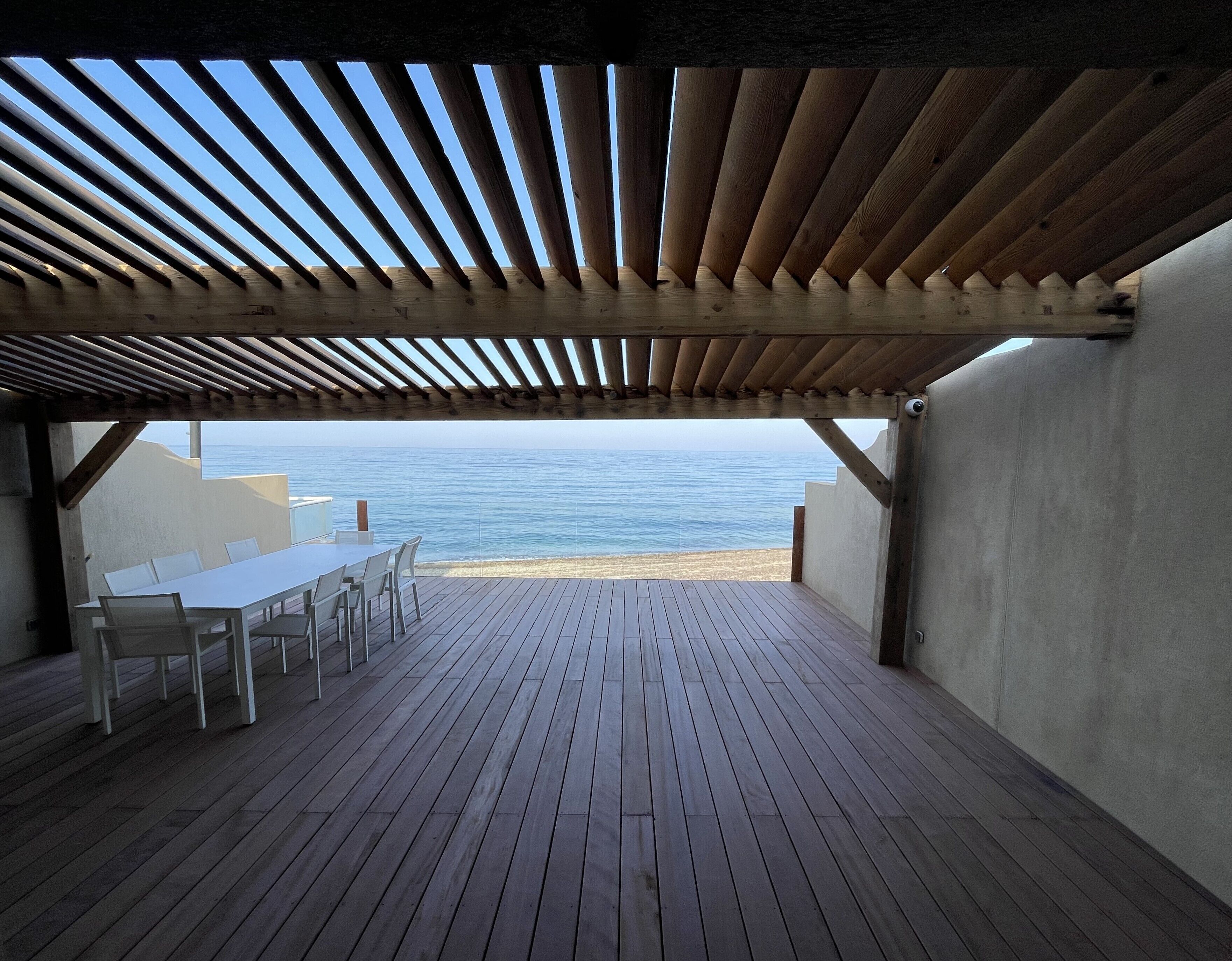 Una terraza de madera al aire libre con una mesa y sillas, con vistas a una playa y al mar.