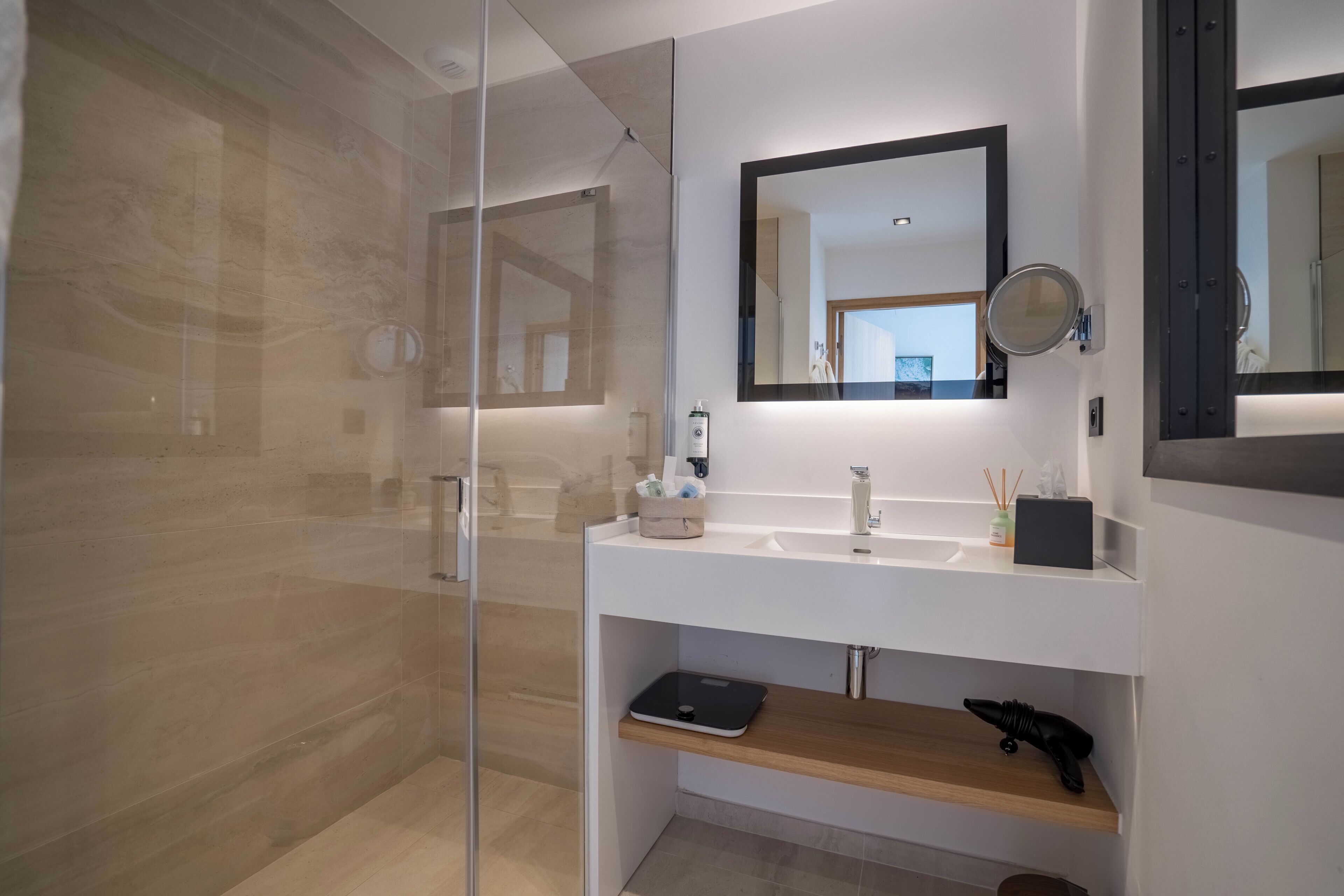 Ein modernes Badezimmer mit einer Duschkabine aus Glas, einem weißen Waschbecken mit Spiegel darüber und einem Holzboden darunter.