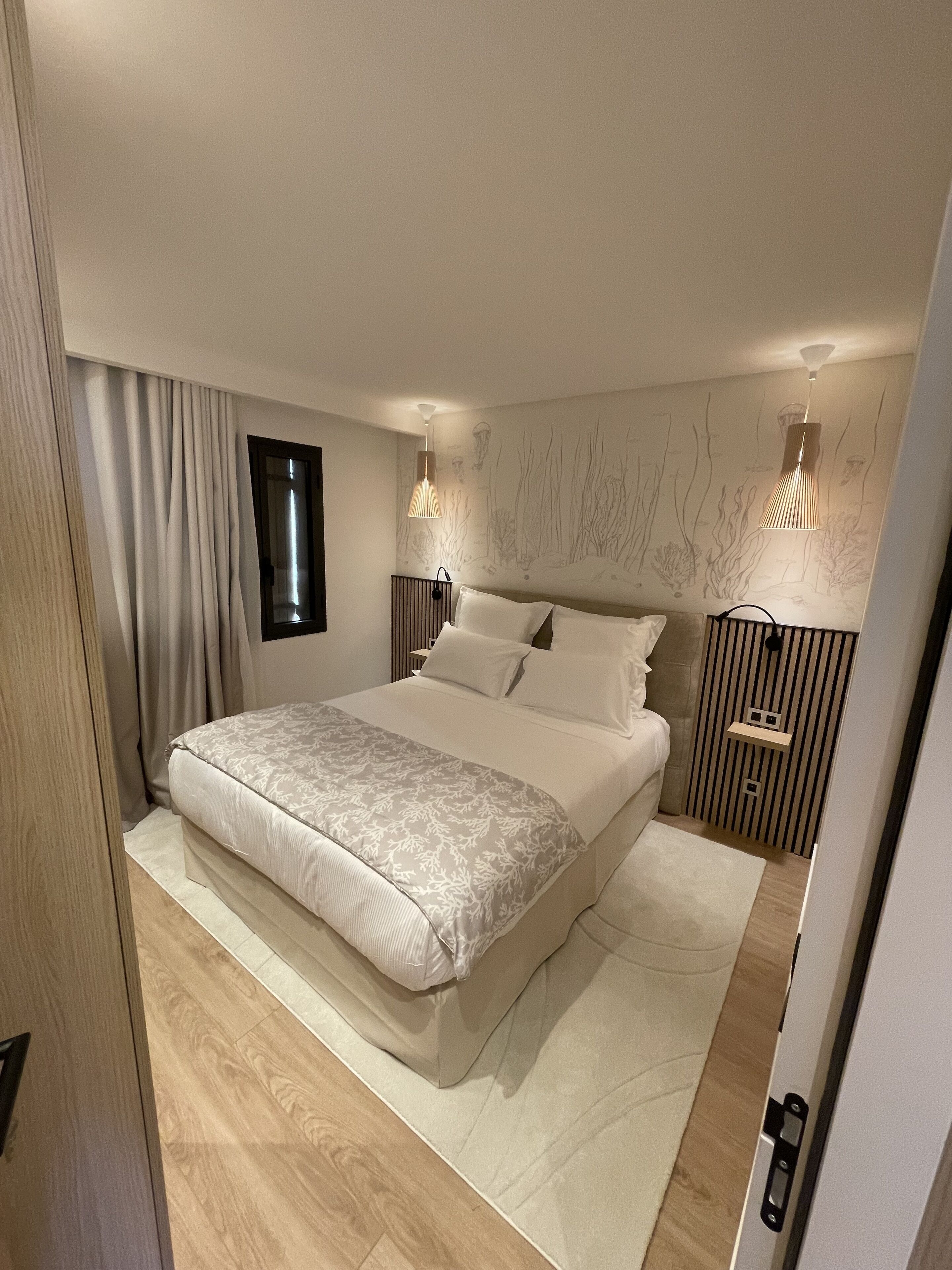 Un dormitorio moderno con una cama grande, dos mesitas de noche con lámparas, una ventana y un mural en la pared.