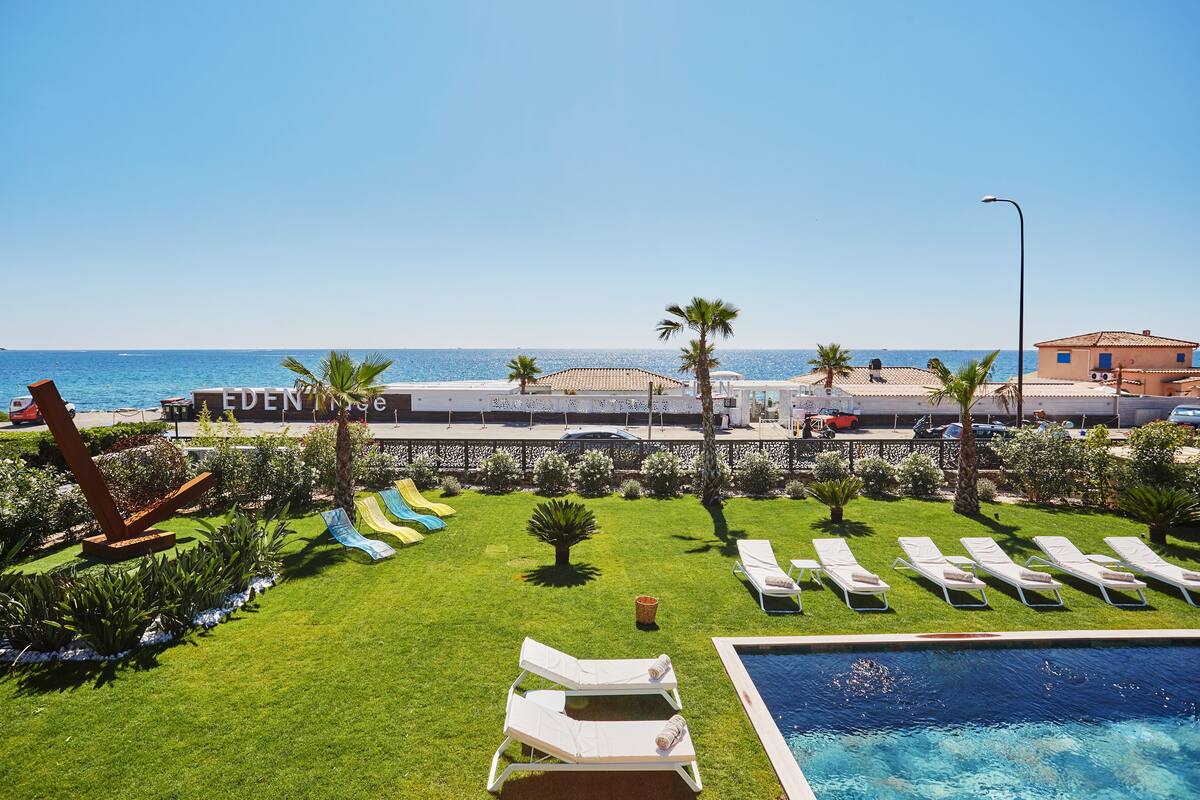 A pool area with lounge chairs, a small pool, and a view of the sea.
