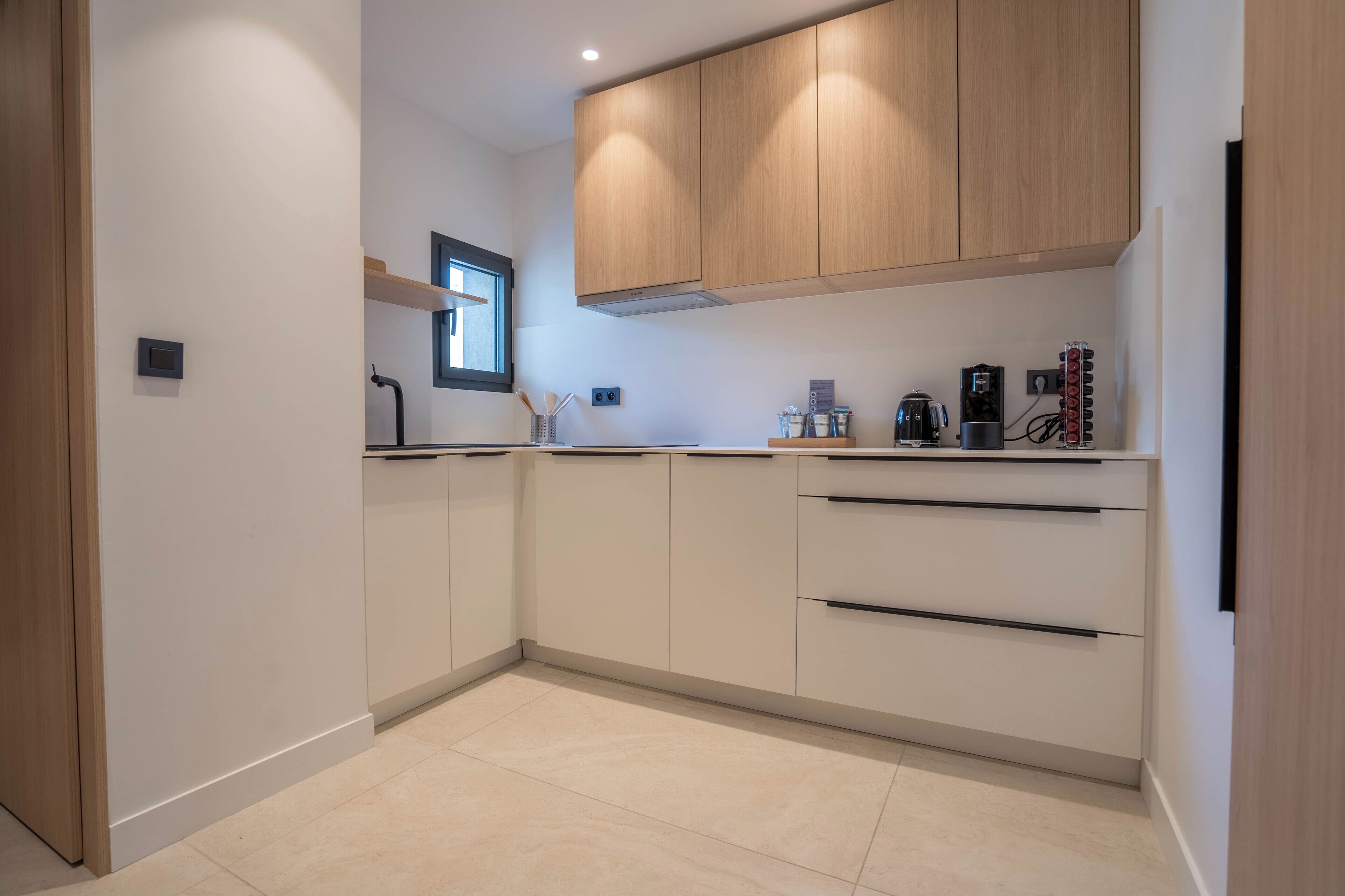 A modern kitchen with white cabinets, a window, and a coffee machine.