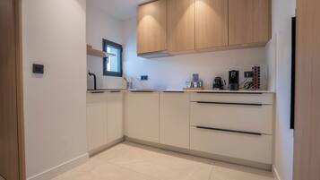 A modern kitchen with white cabinets, a window, and a coffee machine.