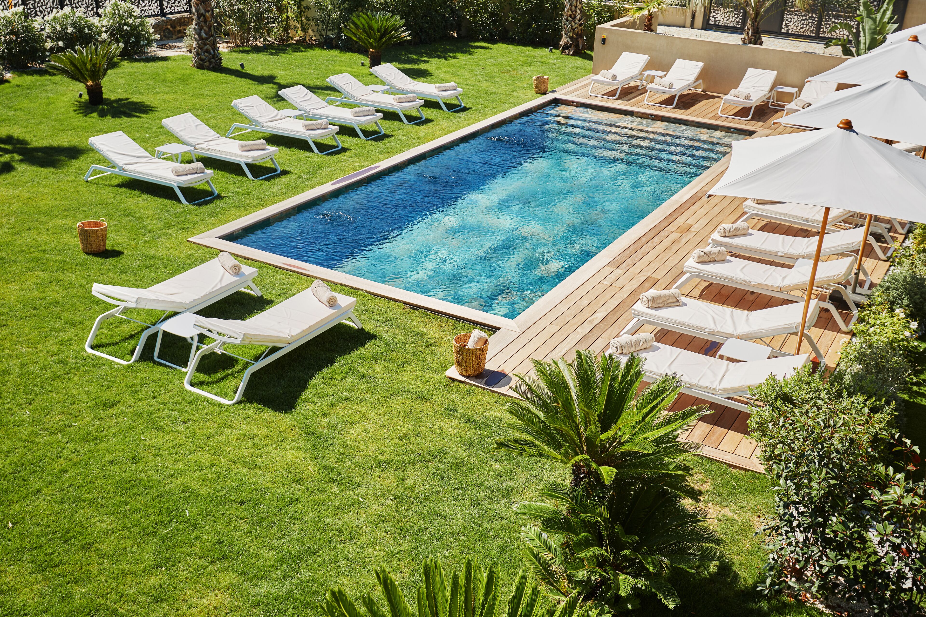 A rectangular swimming pool with a wooden deck and white lounge chairs.