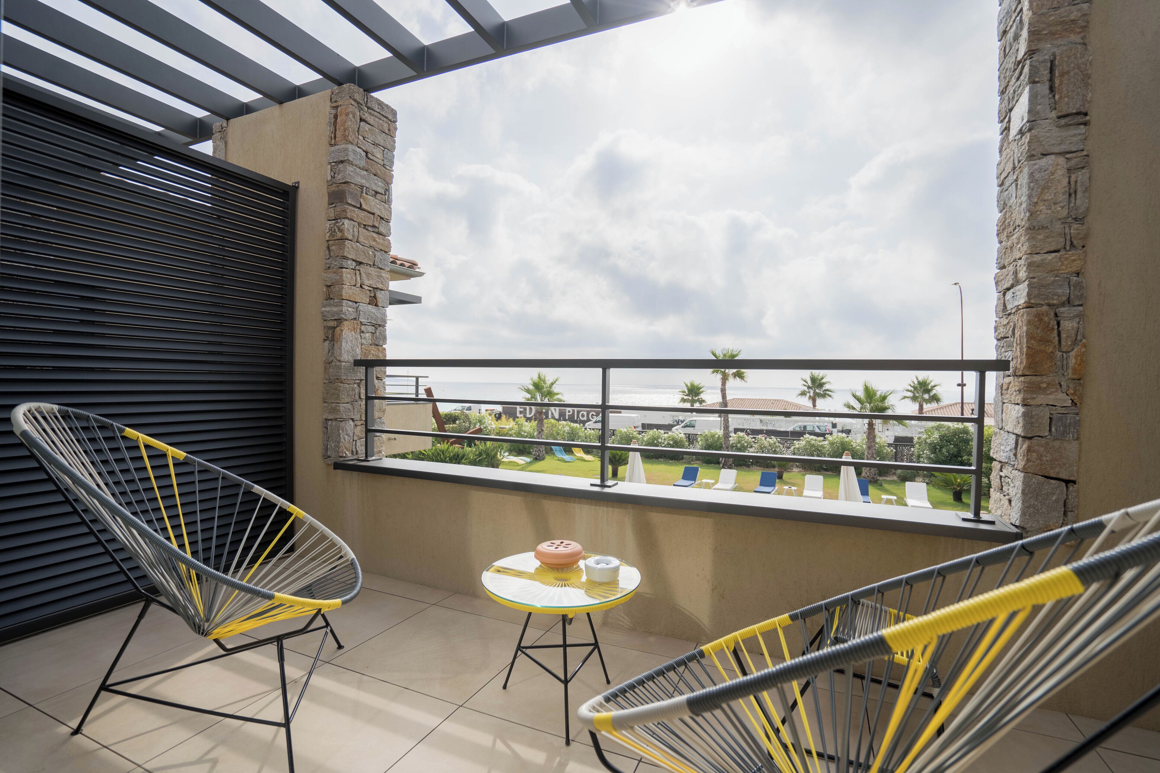 A balcony with two chairs, a small table, and a view of a pool and greenery.
