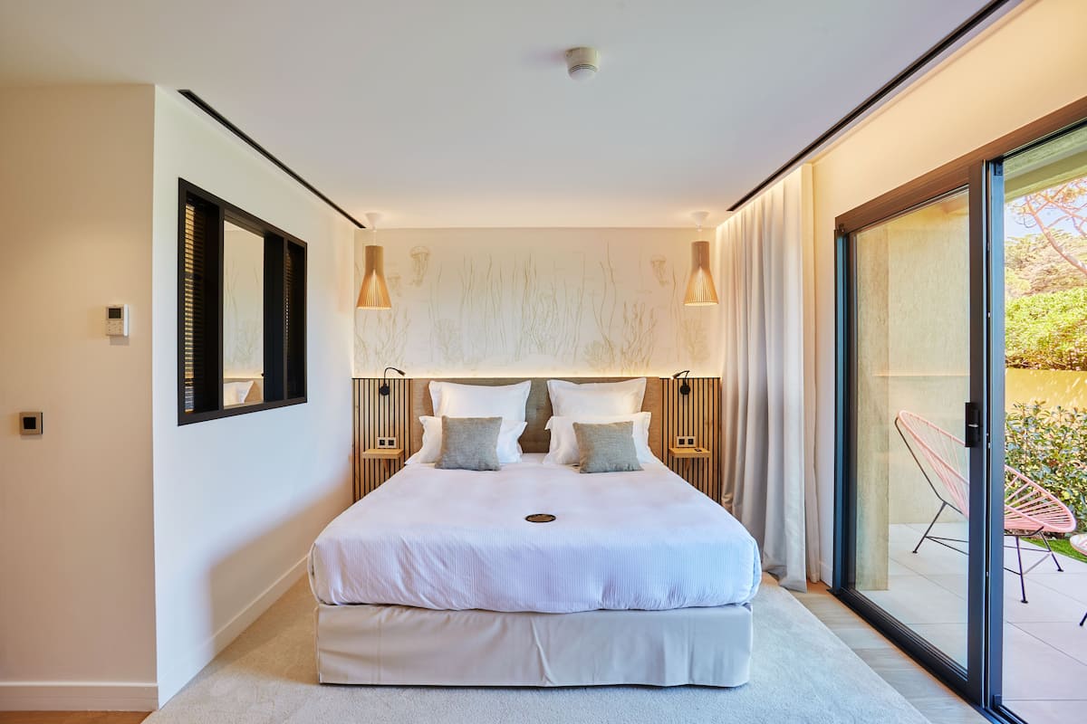A modern bedroom with a large bed, bedside lamps, and a sliding glass door leading to an outdoor area.