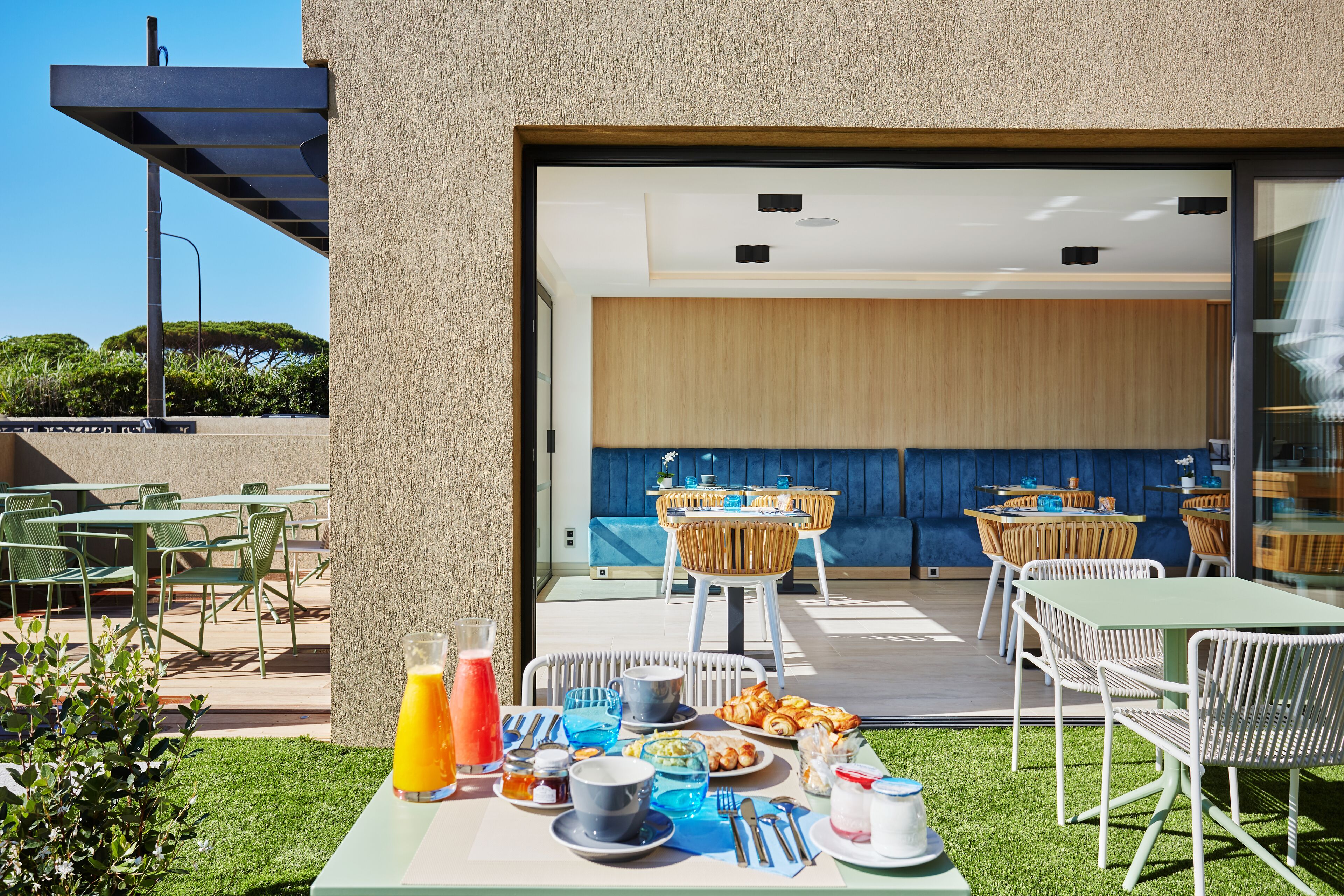 Un espacio de comedor al aire libre con mesas y sillas, una disposición tipo bufé y vistas al interior a través de un vidrio.