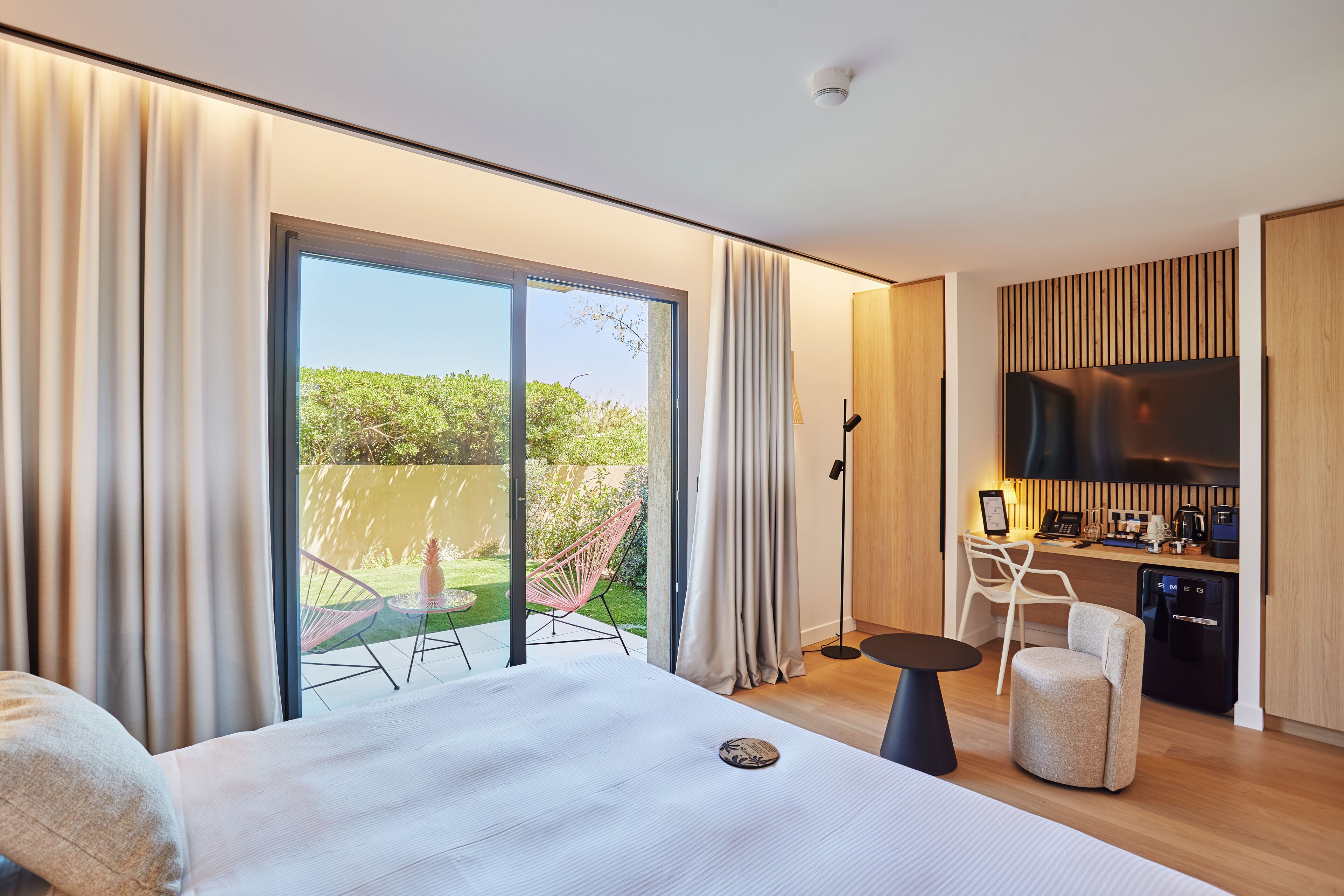 A modern hotel room with a large bed, a desk, a television, and a kitchenette.
